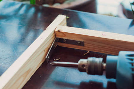 Woodworking with a drill to screw angle bracket in a wooden block with wood shavings and smoke in a...