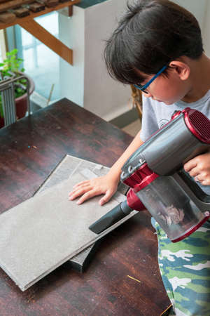 A young boy is cleaning the air filter sheet with the vacuum.の写真素材