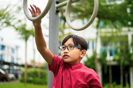 Young asian children hang on the monkey bar. To exercise at outdoor playground in the neighbourhood.