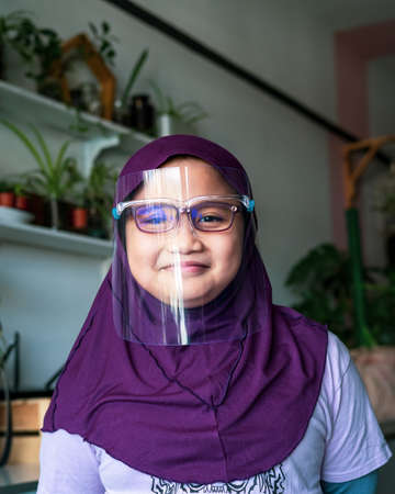 A young girl in hijab wearing the face protection shield.