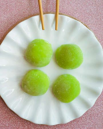 Japanese dessert with Malaysian fusion, Pandan mochi in green colour on a white plate with chopsticks.の写真素材