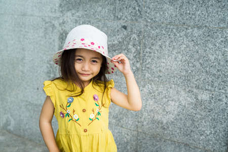 Portrait of beautiful little gorgeus lovely toddler girl in mustard summer look clothes, fashion dress, and hat. Happy healthy asian child posing in outdoor.の写真素材