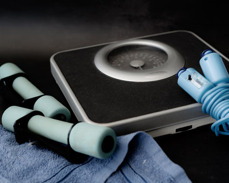 weight scale, pair of weights dumbbells with skipping rope with pedometer on dark background.