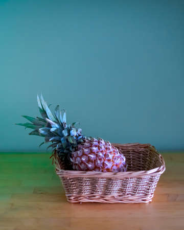 single whole pineapple in a basket on a wooden table at the green cabinet background.の写真素材