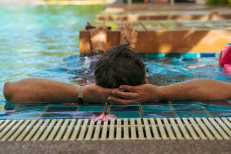Back view of a tanned colour man relaxing in the swimming pool. Summer vacationの写真素材