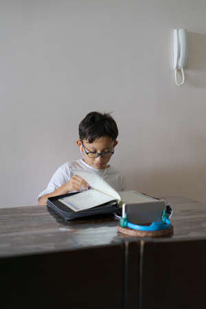 Asian kid reading Al-Quran through video call during education and learning from home for kid....