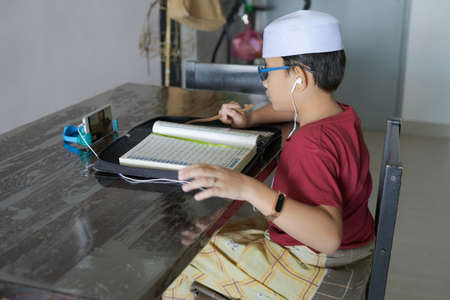 Asian kid reading Al-Quran through video call during education and learning from home for kid....