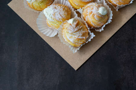 Cream puffs filled with pastry cream and sprinkled with powdered sugar on a dark background.