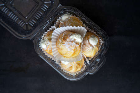 Cream puffs filled with pastry cream and sprinkled with powdered sugar in a transparent clear container.の写真素材
