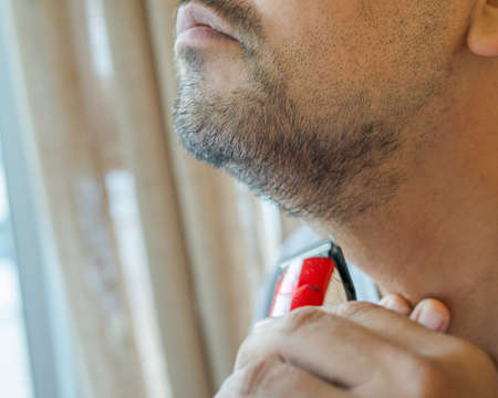 Asian man shaving beard with electric razor machine.の写真素材