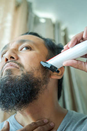 Asian man shaving beard with electric razor machine. Low angle view.の写真素材