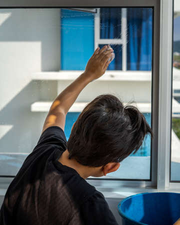The concept of home apartment cleaning. A boy on the window and wipes with a rag. view from behind.の写真素材