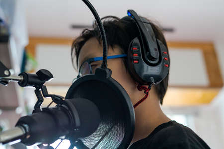 Unidentified young boy recording at home in front of a microphone wearing headphones in a close up low angle portraitの写真素材