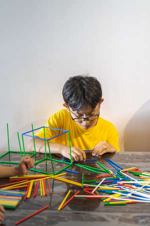 A young boy is constructing colorful plastic sticks with glue gun. fun with building geometric...