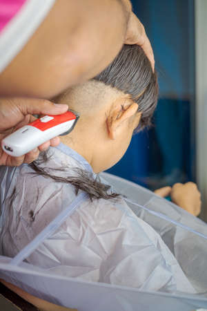 Asian child getting haircut at home from the father. Young boy save his head using electric razor.の写真素材