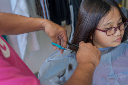 Asian young girl wearing glasses getting haircut at home from the father.