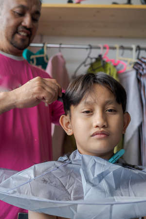 Asian child getting haircut at home from the father.の写真素材