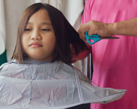 Asian young girl is getting haircut at home from the father. Young teenage girl.の写真素材