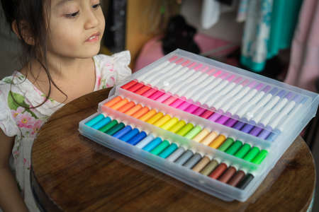 Little girl looking at her colorful markers in transparent plastic packaging.