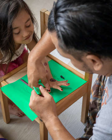 Father painting henna ornaments on daughter's hand.の写真素材