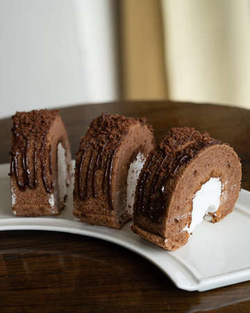 Chocolate roll with fresh cream on a white plate and wooden background