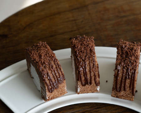 Chocolate roll with fresh cream on a white plate and wooden background