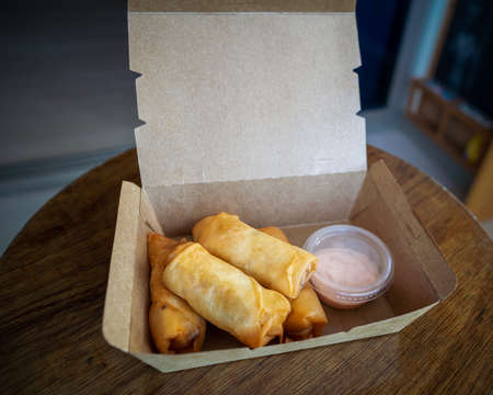 Fried spring rolls in a brown takeaway container with creamy sauce.