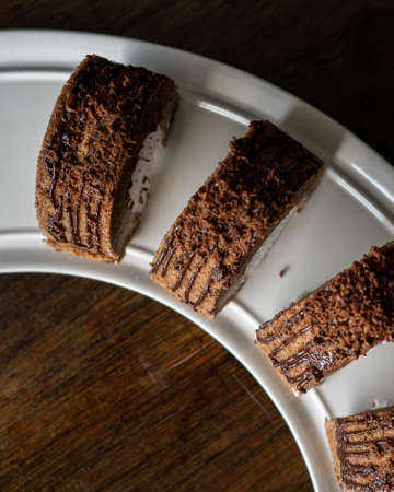 Chocolate roll with fresh cream on a white plate and wooden background