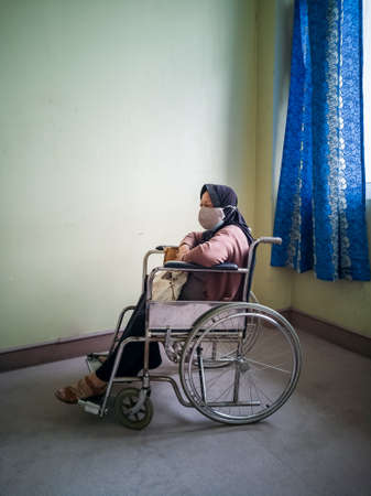 Portrait of a senior woman wearing hijab on wheelchair in a hospital.の写真素材
