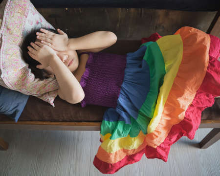 A cute little girl lying on the long chair in the living-room. Covering eyes with hands.の写真素材