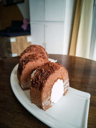 Chocolate roll with fresh cream on a white plate and wooden backgroundの写真素材