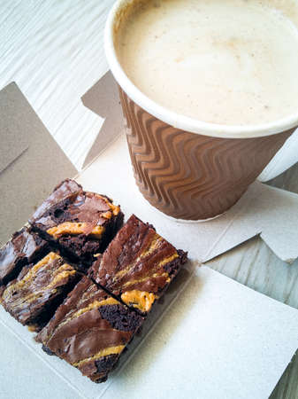 Freshly baked brownies with hot and cold latte in a takeaway cups.の写真素材