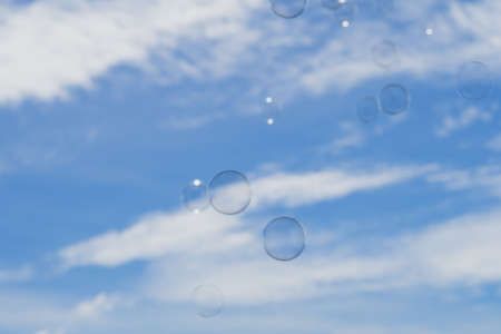 Blurry photo of the floating soap bubbles and blue skies with clouds.