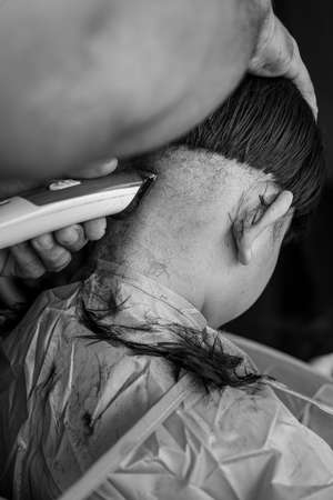 Asian child getting haircut at home from the father. View from behind. Monochrome, black and white.の写真素材