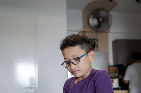 Portrait of young boy wearing glasses looking down at home. Low angle view.の写真素材