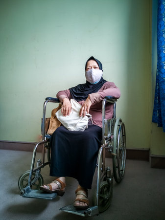 Portrait of a senior woman wearing hijab on wheelchair in a hospital.の写真素材