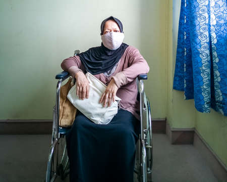 Portrait of a senior woman wearing hijab on wheelchair in a hospital.