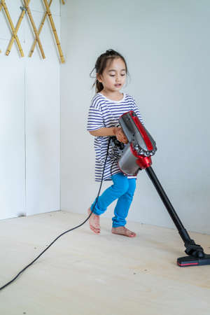 Cute little girl cleaning wooden floor with vacuum cleanerの写真素材
