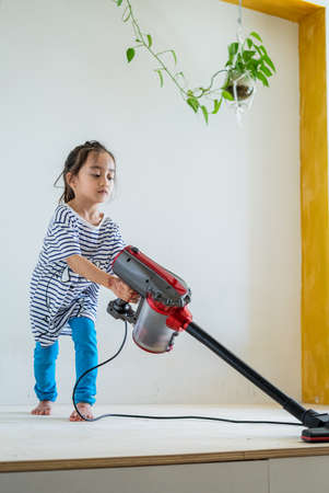 Cute little girl cleaning wooden floor with vacuum cleanerの写真素材