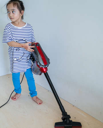 Cute little girl cleaning wooden floor with vacuum cleanerの写真素材