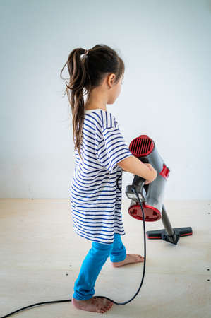 Cute little girl cleaning wooden floor with vacuum cleaner