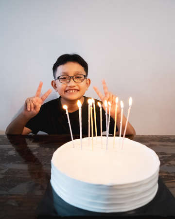 Young asian boy wearing glasses making peace sign while celebrating birthday cake.の写真素材