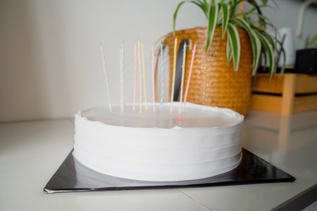 White cake with candles and blank background space on black cake board and wooden greenery background, birthday cake mockupの写真素材