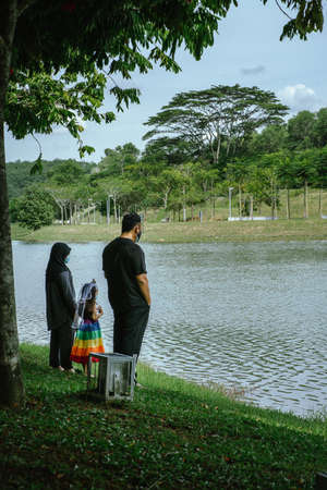 Back view of a father and his little daughter wearing face masks and standing at the lake's park.の写真素材