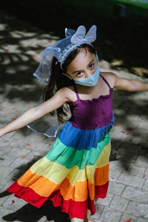 Little girl wearing face mask with rainbow dress enjoying outdoor in the park. New normal.の写真素材