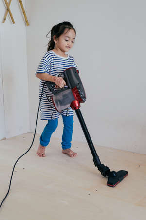 Cute little girl cleaning wooden floor with vacuum cleanerの写真素材
