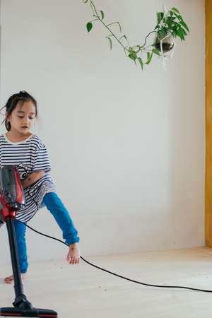 Cute little girl cleaning wooden floor with vacuum cleanerの写真素材