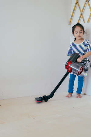 Cute little girl cleaning wooden floor with vacuum cleanerの写真素材