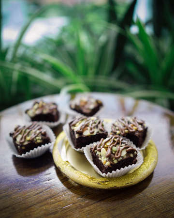 Chocolate brownie cubes with chocolate drizzle in paper cups on a wooden background.の写真素材