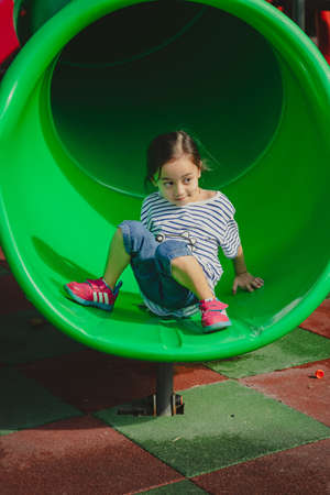 Little girl playing at the playground. Sitting at the end of the slide.の写真素材